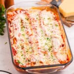 Baked manicotti covered in tomato sauce, melted mozzarella cheese, and garnished with chopped parsley in a glass baking dish. The cheese is slightly browned and bubbly on top.