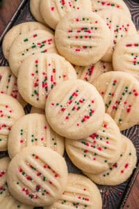 Whipped shortbread cookies with fork marks and is topped with red, green, and white nonpareil sprinkles.