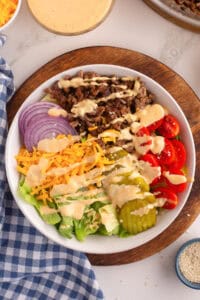Burger bowl with ground beef, pickles, tomatoes, cheese, onion, lettuce, and creamy burger sauce dressing.