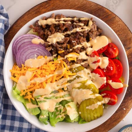 Burger bowl with ground beef, pickles, tomatoes, cheese, onion, lettuce, and creamy burger sauce dressing.