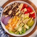 Top-down view of a burger bowl with seasoned ground beef, pickles, cheese, tomato, onion, and a drizzle of homemade burger sauce.