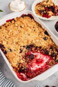 Baked cherry cobbler in a white rectangular dish, showing a golden crumbly topping and a missing portion revealing cherry filling.