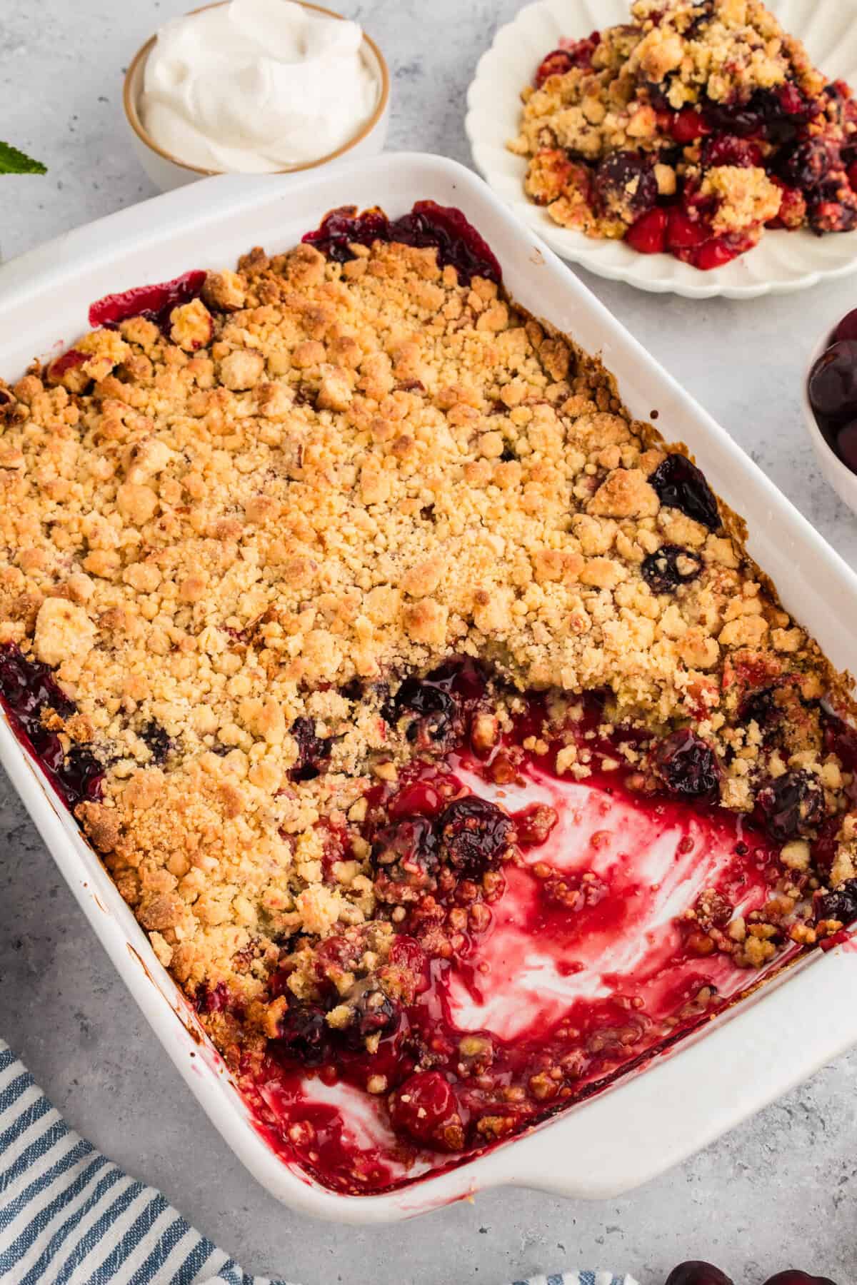 Baked cherry cobbler with yellow cake mix in a white rectangular dish, showing a golden crumbly topping and a missing portion revealing cherry filling.
