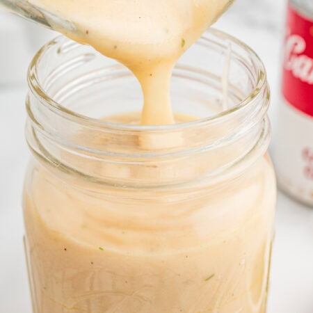 Cream of chicken soup being poured into a mason jar with a can of condensed cream of chicken soup in the background.