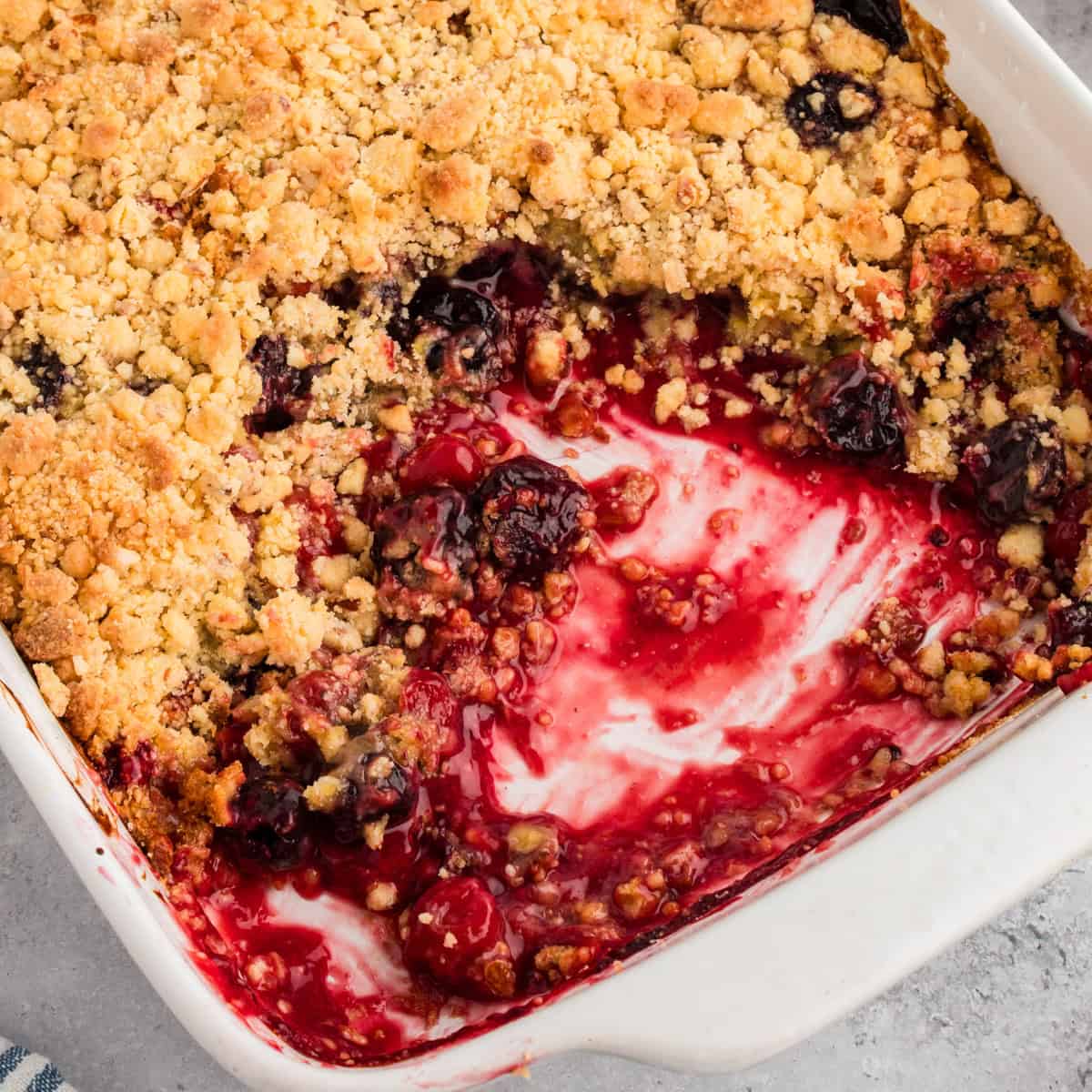 Cherry cobbler with cake mix in a white baking dish, showing a golden crumbly topping and a cherry filling.
