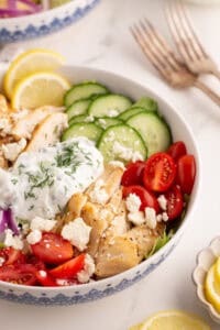 Chicken gyro bowl with sliced vegetables, tzatziki sauce, and lemon slices.