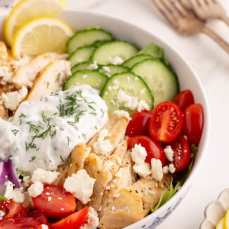Chicken gyro bowl with sliced vegetables, tzatziki sauce, and lemon slices.