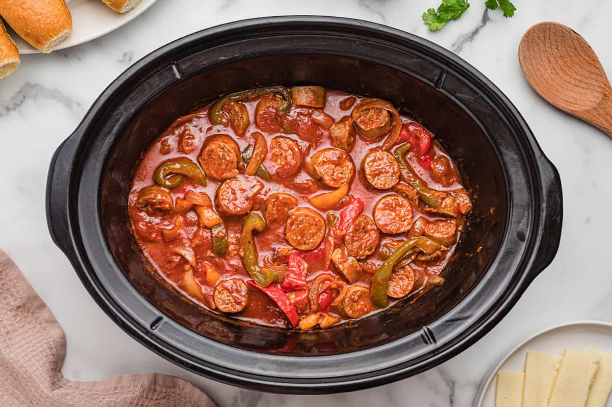 Top-down view of sausage and peppers in sauce inside a slow cooker.