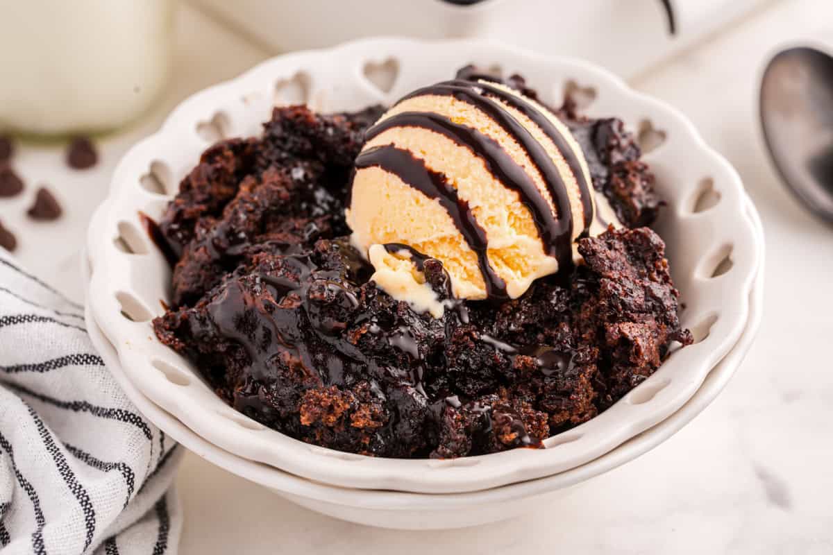 Chocolate pudding cake with vanilla ice cream and chocolate drizzle in a bowl.
