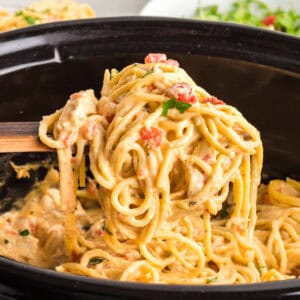 Creamy chicken spaghetti lifted from a slow cooker on a wooden spoon.
