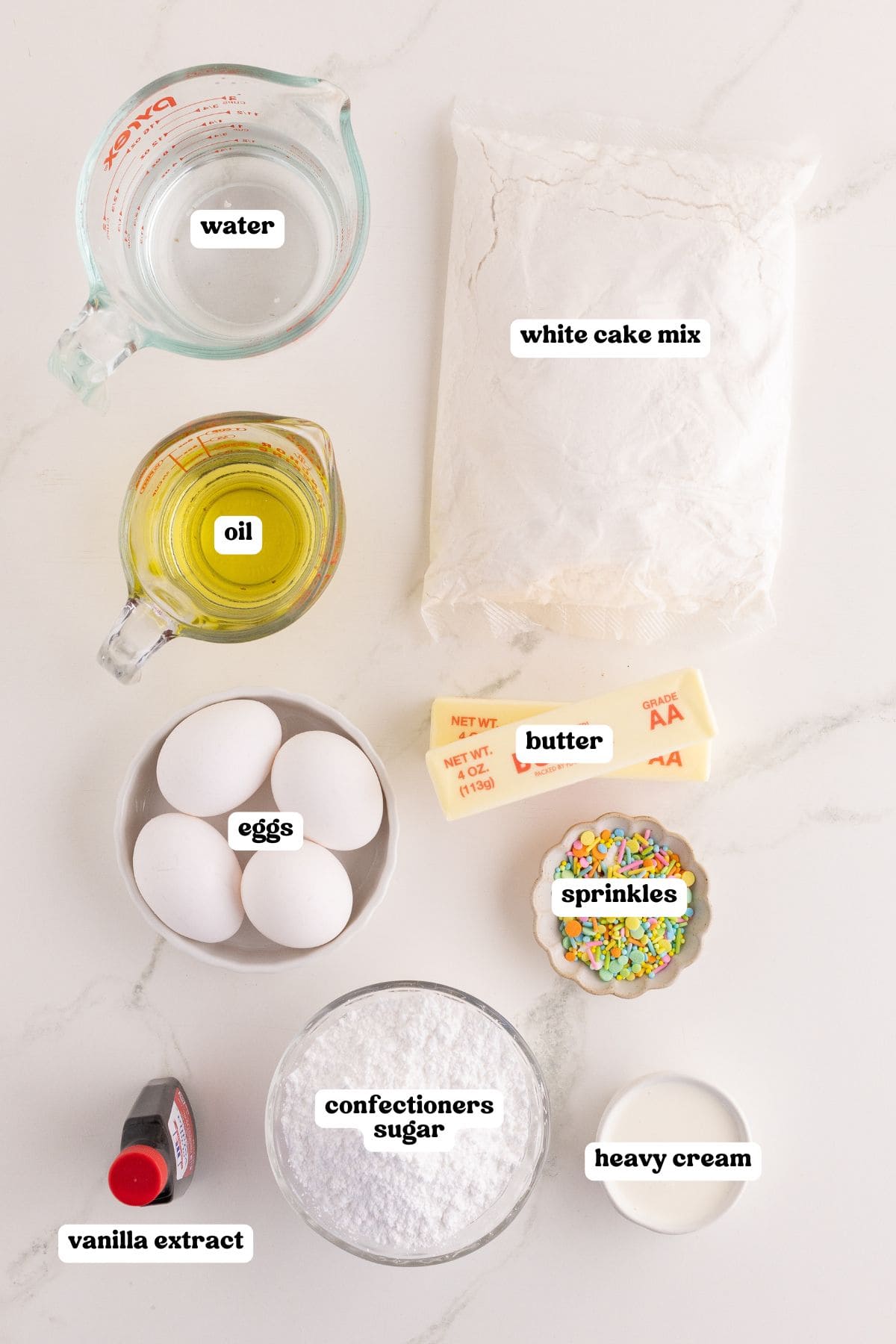 Ingredients for bunny cake labeled: water, oil, a bag of white cake mix, eggs, butter, pastel sprinkles, confectioners sugar, heavy cream, and vanilla extract.