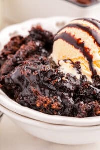 Chocolate pudding cake topped with vanilla ice cream and chocolate sauce in a white bowl.