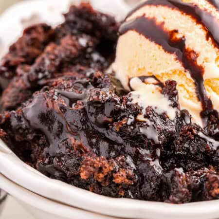 Chocolate pudding cake topped with vanilla ice cream and chocolate sauce in a white bowl.