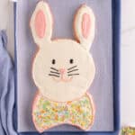Easter bunny cake with white frosting and pink ear details, piped face, and bow tie.
