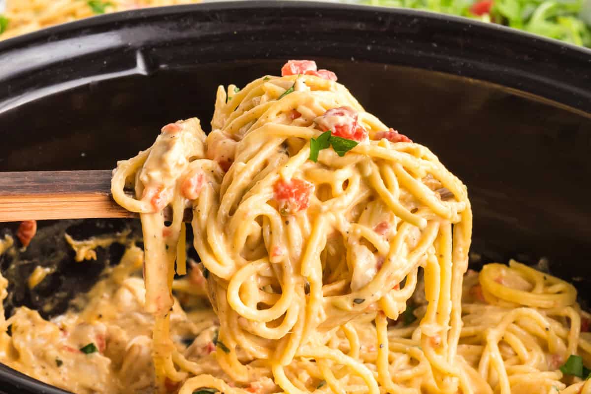 Creamy chicken spaghetti lifted from a slow cooker on a wooden spoon.