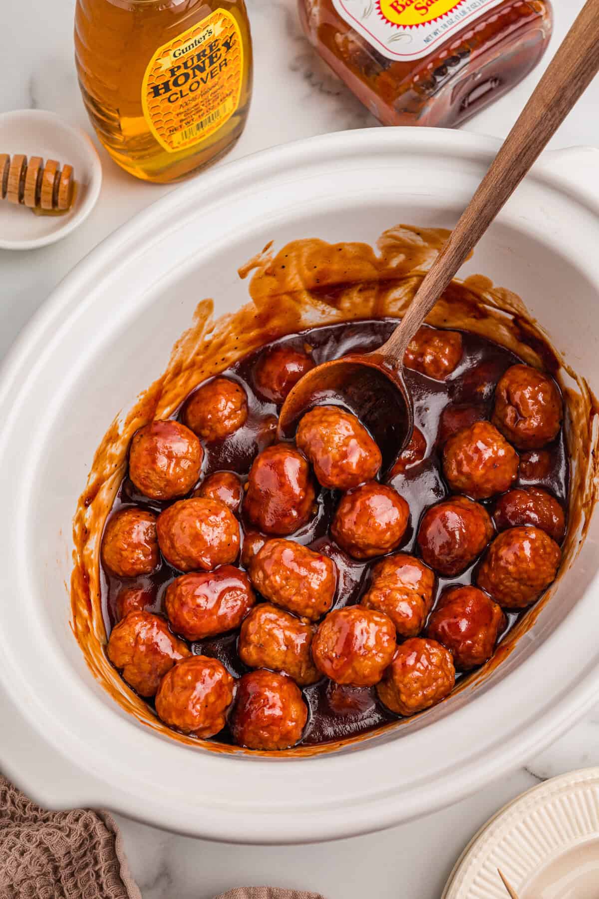 Honey BBQ crockpot meatballs coated in sauce inside a slow cooker with a wooden spoon.Meatballs coated in sauce inside a slow cooker with a wooden spoon.