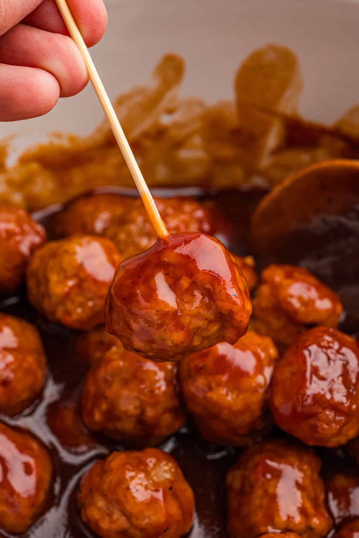 Close-up of a toothpick holding a honey bbq meatball above others in a crockpot.