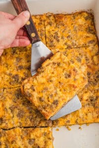 A square slice of sausage breakfast casserole being lifted from the pan with a metal spatula.