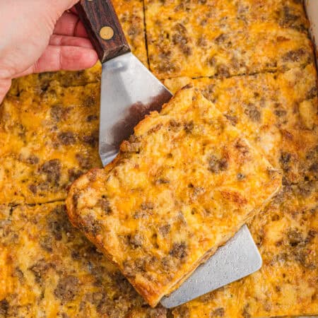 A square slice of sausage breakfast casserole being lifted from the pan with a metal spatula.