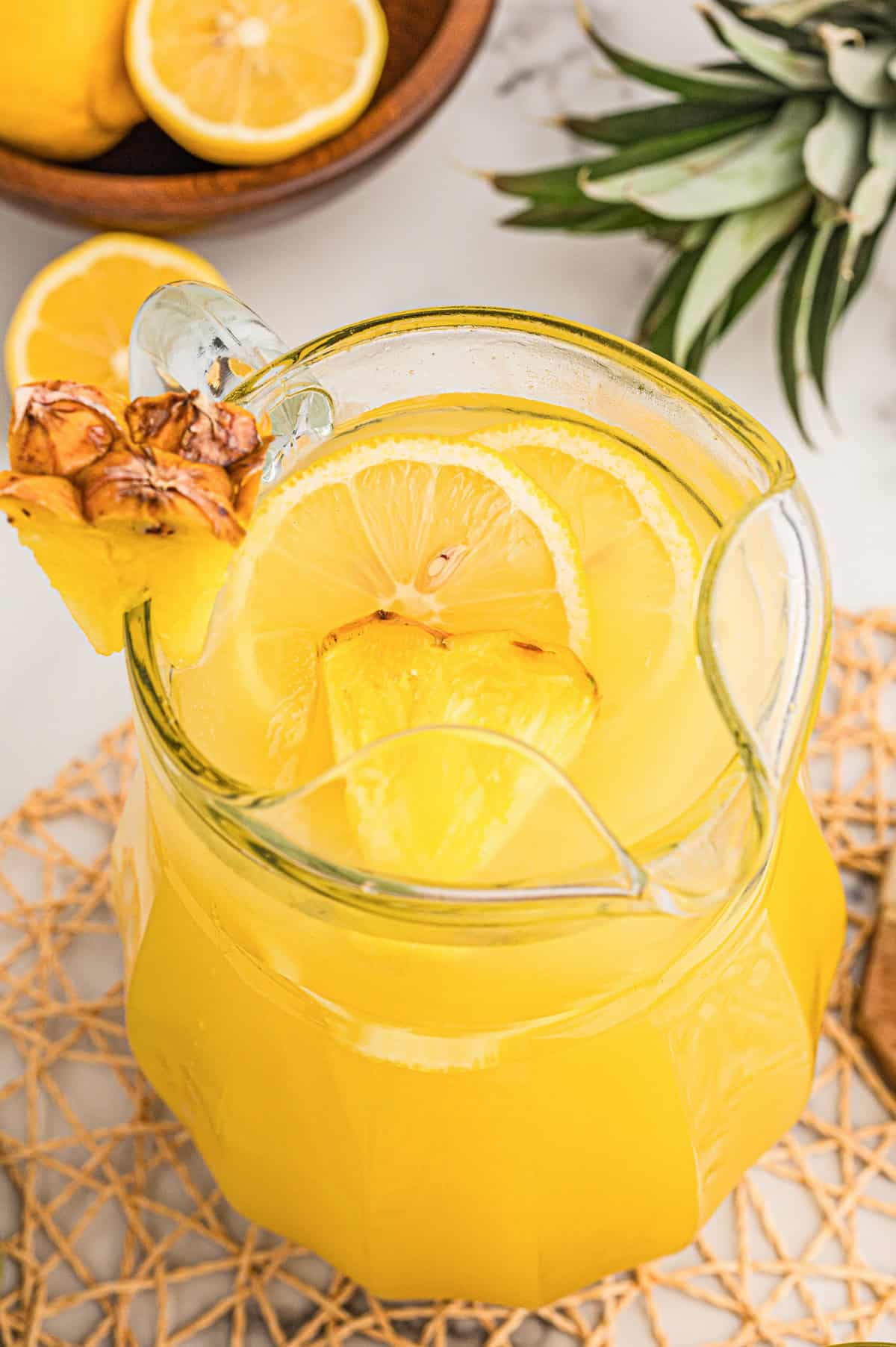 Pitcher of country time lemonade pineapple punch with lemon slices and pineapple pieces seen from above.