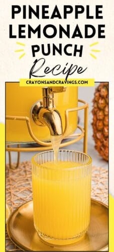 Close-up of yellow pineapple lemonade punch pouring from a gold spout into a ribbed glass. The drink dispenser sits in a gold stand, with part of a pineapple visible in the background. Text reads: “Pineapple Lemonade Punch Recipe. crayonsandcravings.com.”