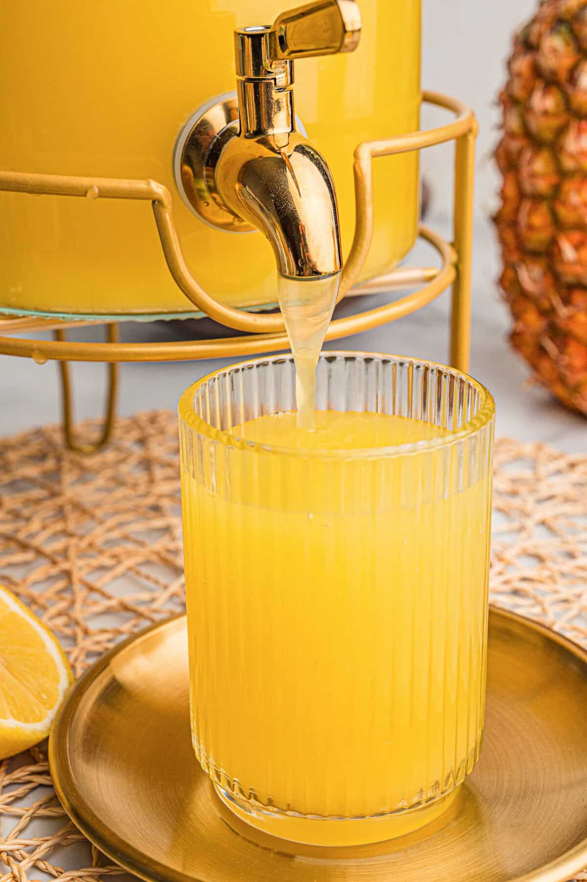 Pineapple lemonade punch with Sprite pouring from a gold spout into a ribbed glass on a gold tray.