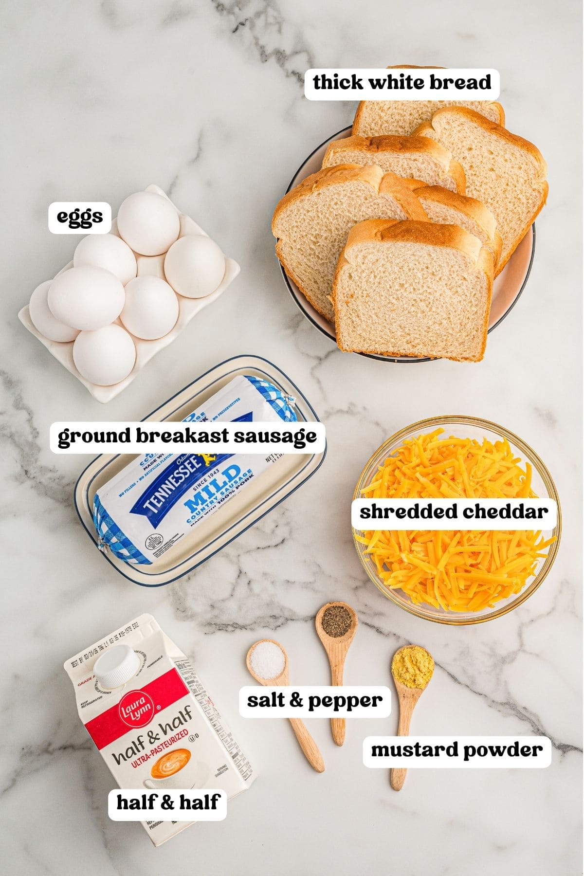 Overhead ingredient photo for sausage breakfast casserole showing eggs, thick white bread, ground breakfast sausage, shredded cheddar, half-and-half, salt, pepper, and mustard powder. Each ingredient is labeled with text on the image.