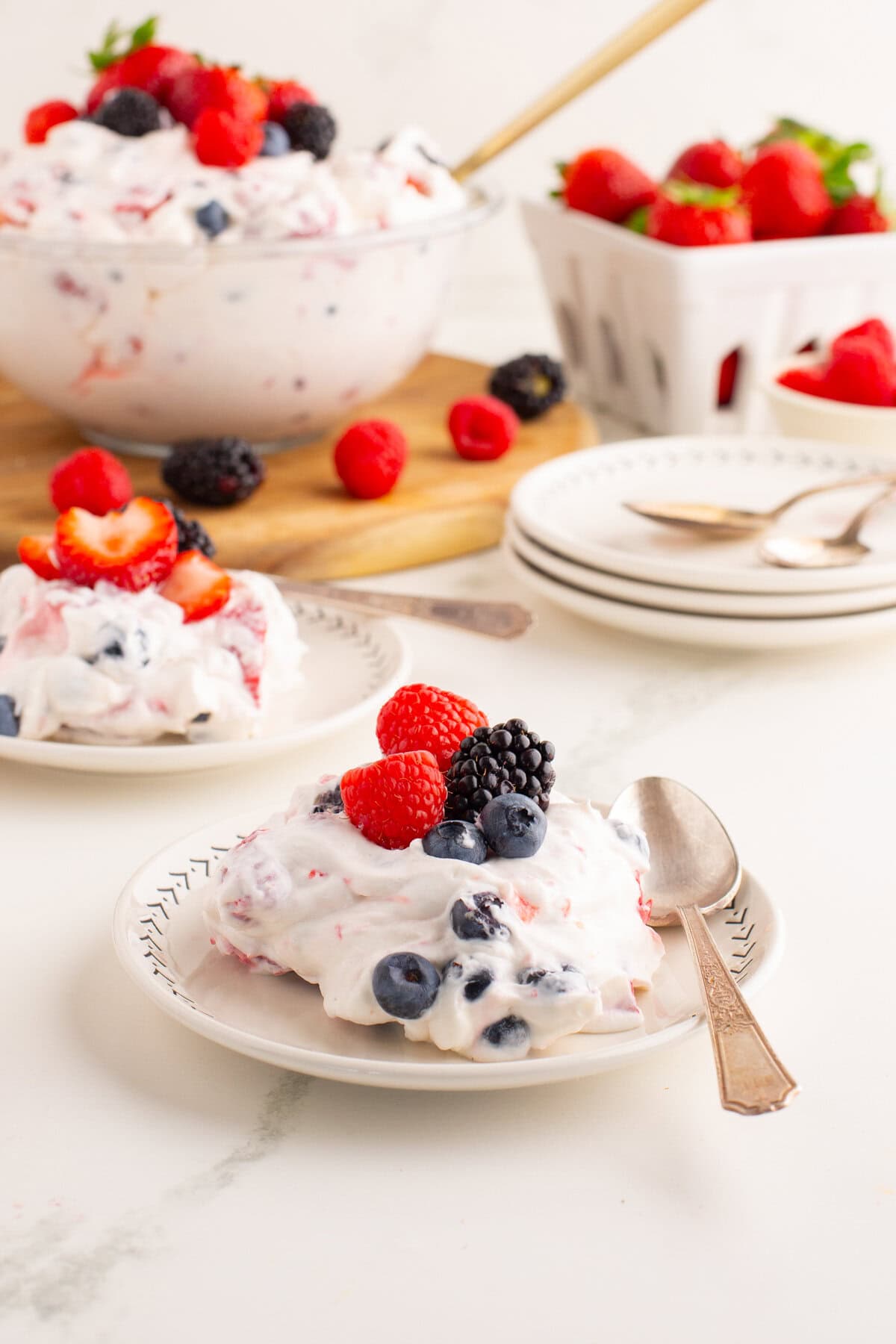 A serving of summer berry cheesecake salad sits on a small plate with a spoon beside it.
