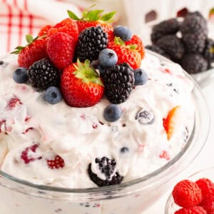 Close-up of a creamy mixed berry cheesecake salad in a glass bowl, topped with strawberries, raspberries, blueberries, and blackberries.