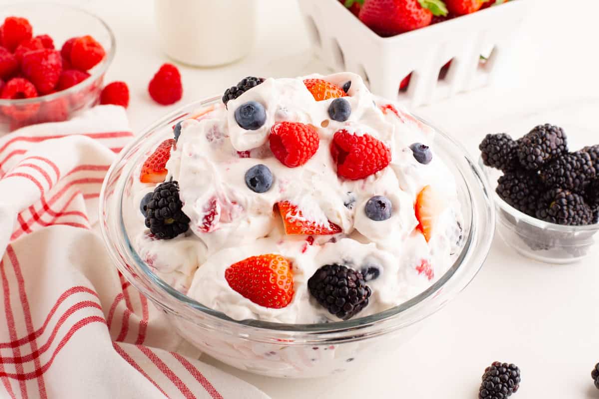 Bowl of berry fluff salad surrounded by fresh berries and a striped cloth.