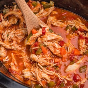 Spoon lifting crock pot chicken paprika coated in a red sauce with visible diced tomatoes from a slow cooker.