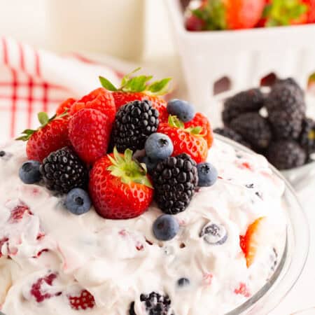 Close-up of a creamy berry cheesecake salad in a glass bowl, topped with strawberries, raspberries, blueberries, and blackberries.