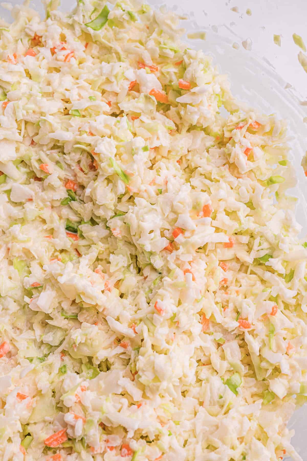 Top-down view of finely shredded cabbage and carrot coleslaw mixed in creamy dressing in a glass bowl.
