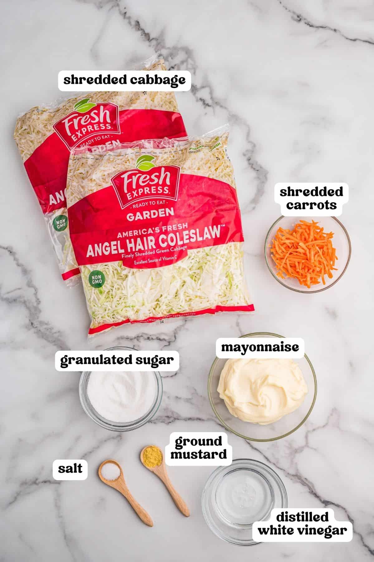 Ingredients on a marble counter: bagged angel hair coleslaw, shredded carrots, sugar, mayonnaise, salt, ground mustard, and white vinegar.