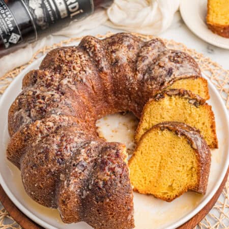 Rum cake with cake mix on a white platter with a bottle of dark rum and a slice cut in the background.