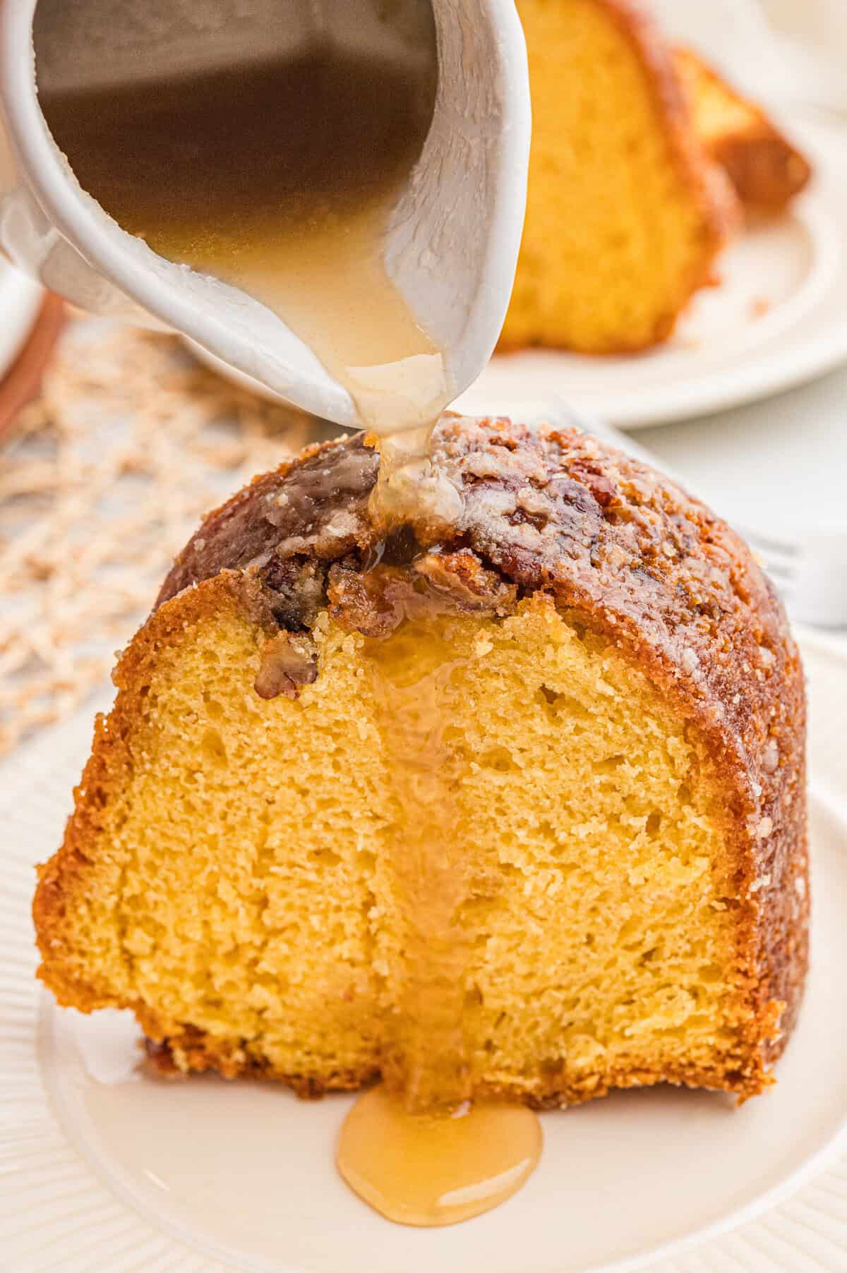 Amber glaze being poured from a small white pitcher onto a slice of rum bundt cake.