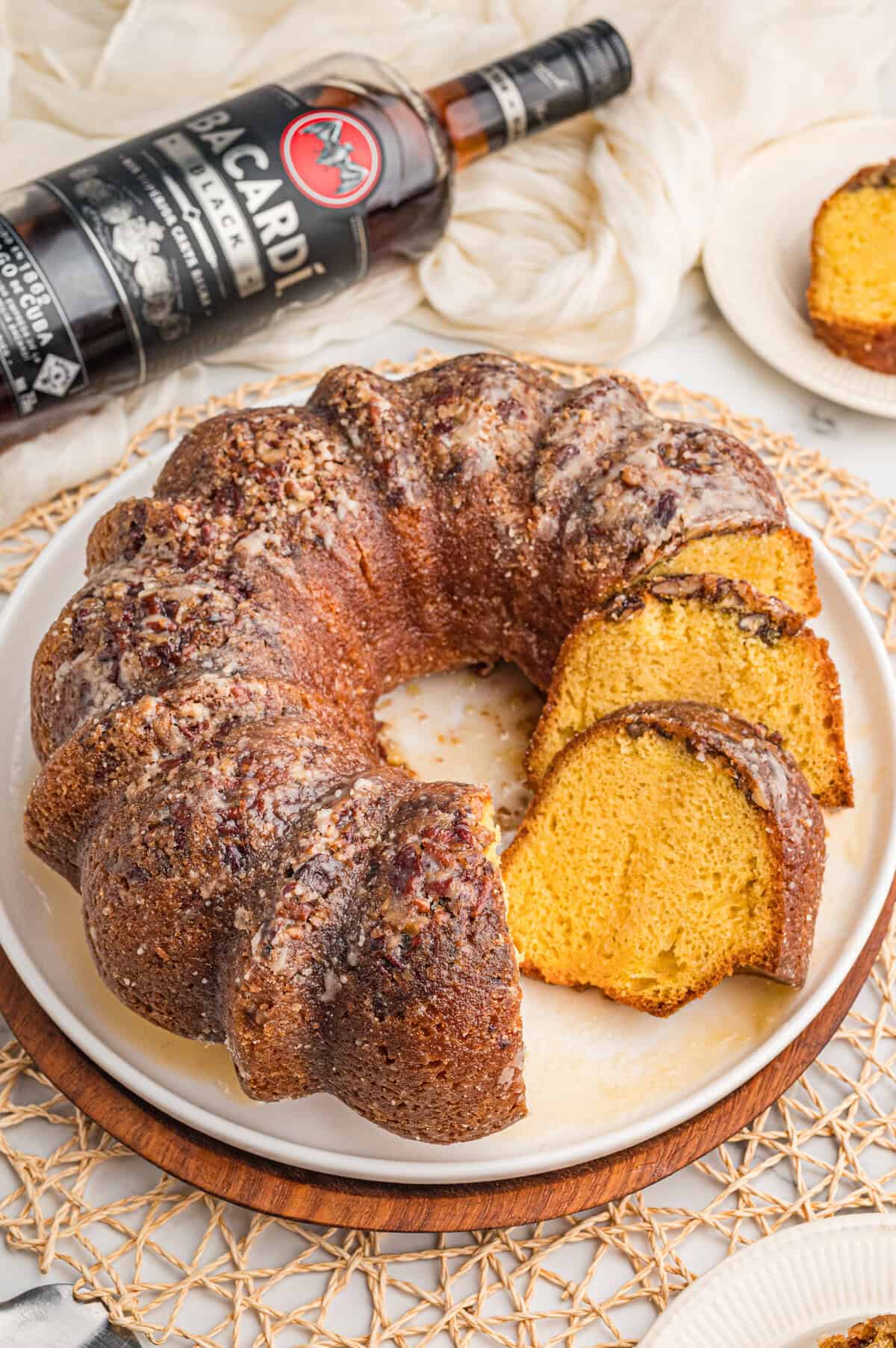 Rum cake with cake mix on a white platter with a bottle of dark rum and a slice cut in the background.