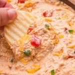 A ruffled potato chip held up with a scoop of dip, diced tomatoes, and shredded cheddar.