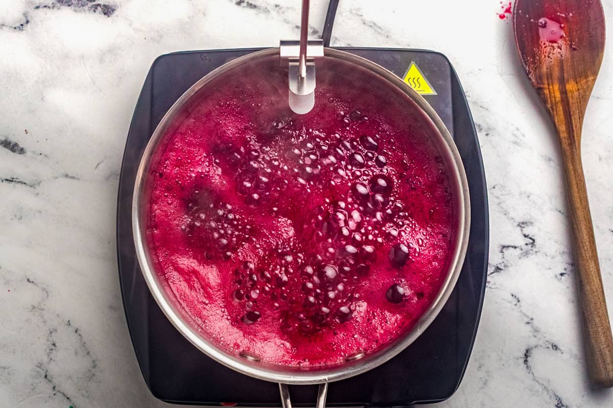 Bubbling blackberry jam in a saucepan with a candy thermometer attached to the rim.