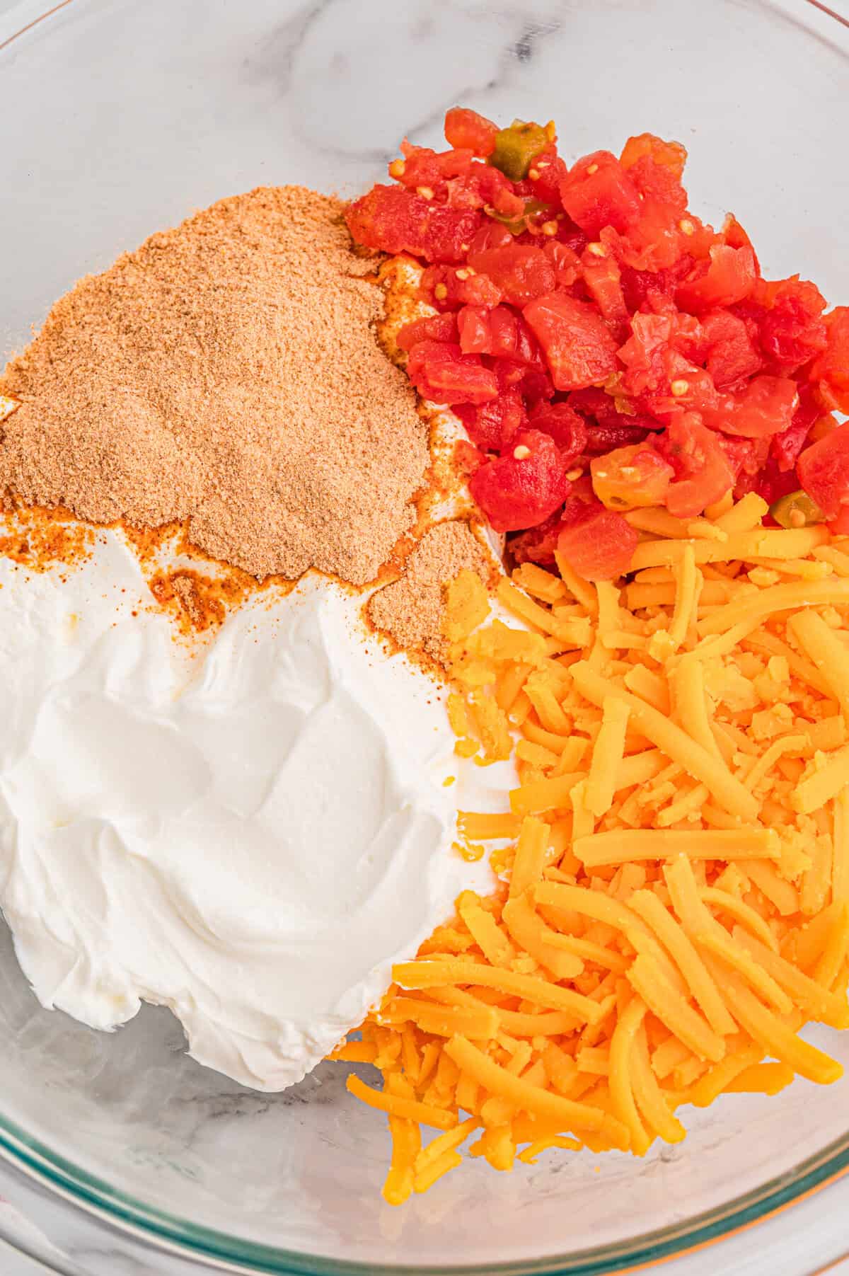 Sour cream, taco seasoning, diced tomatoes with green chilies, and shredded cheddar in a glass mixing bowl.