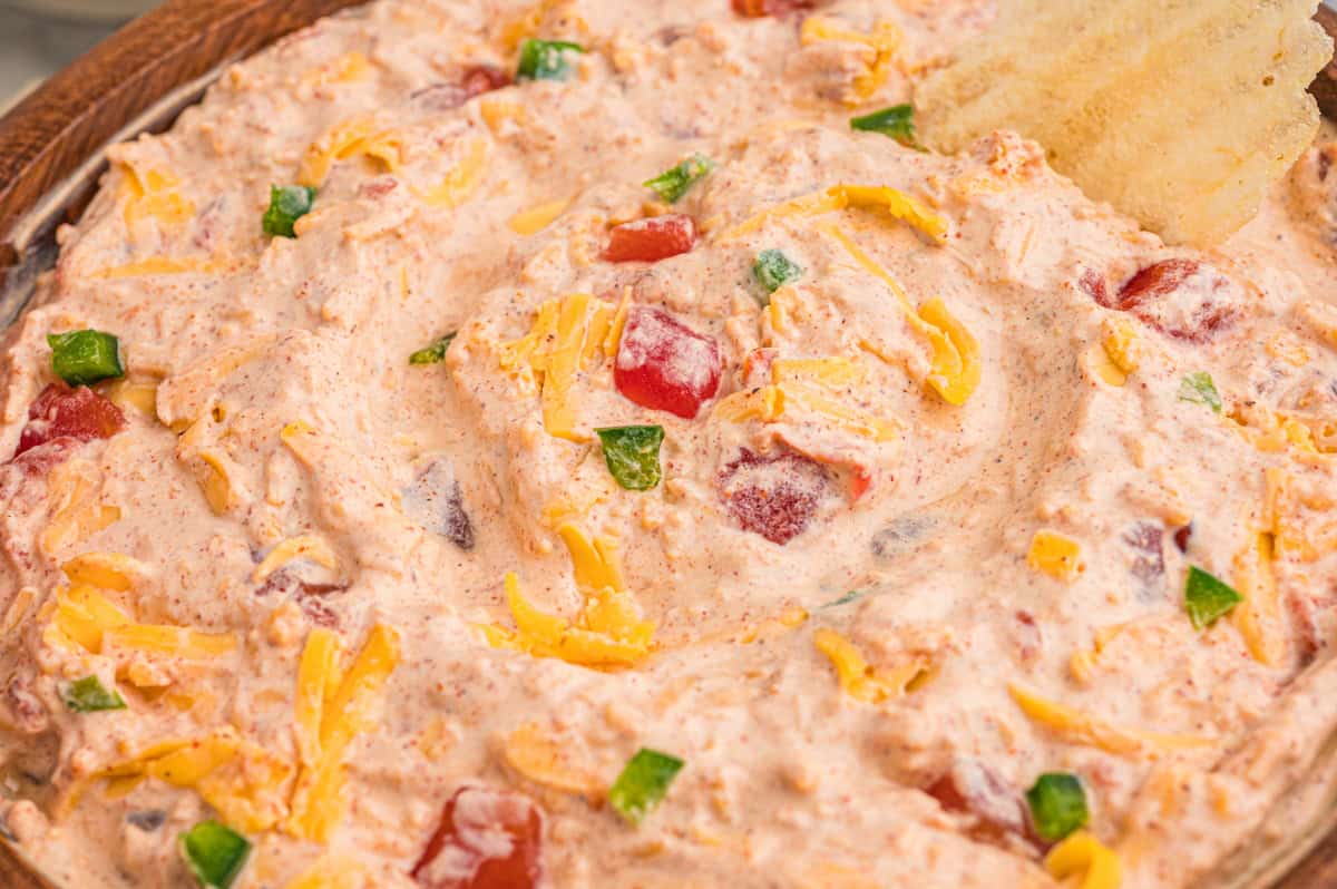 Close-up of creamy dip in a wooden bowl flecked with shredded cheddar, diced tomatoes, and jalapenos.