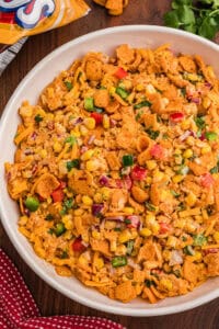 Frito corn salad in a white serving bowl topped with crushed Chili Cheese Fritos, shredded cheddar, and diced red and green bell pepper.