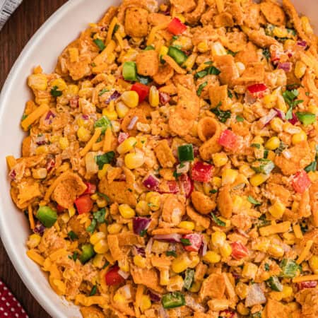 Frito corn salad in a white serving bowl topped with crushed Chili Cheese Fritos, shredded cheddar, and diced red and green bell pepper.