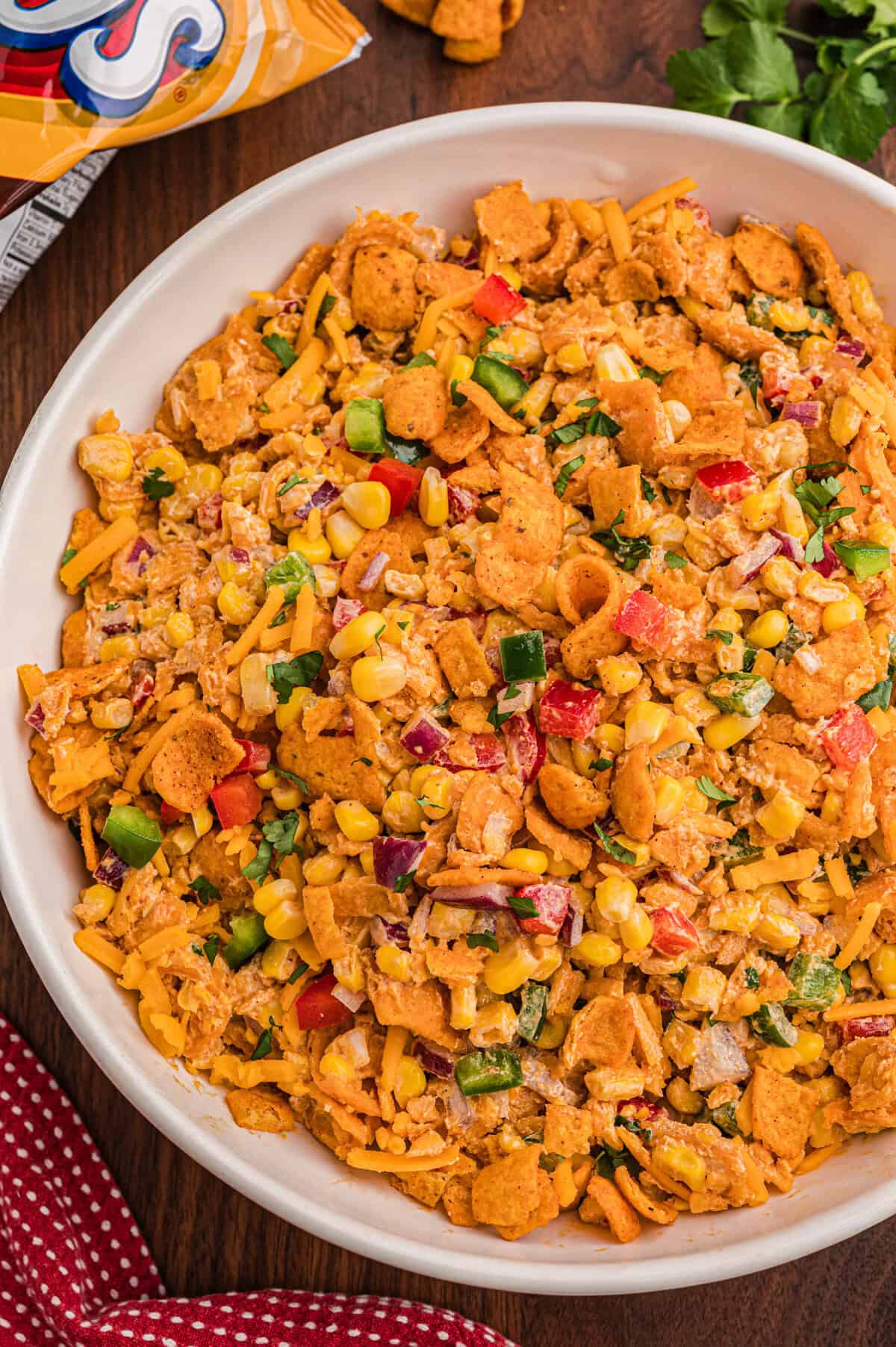 Frito corn salad in a white serving bowl topped with crushed Chili Cheese Fritos, shredded cheddar, and diced red and green bell pepper.