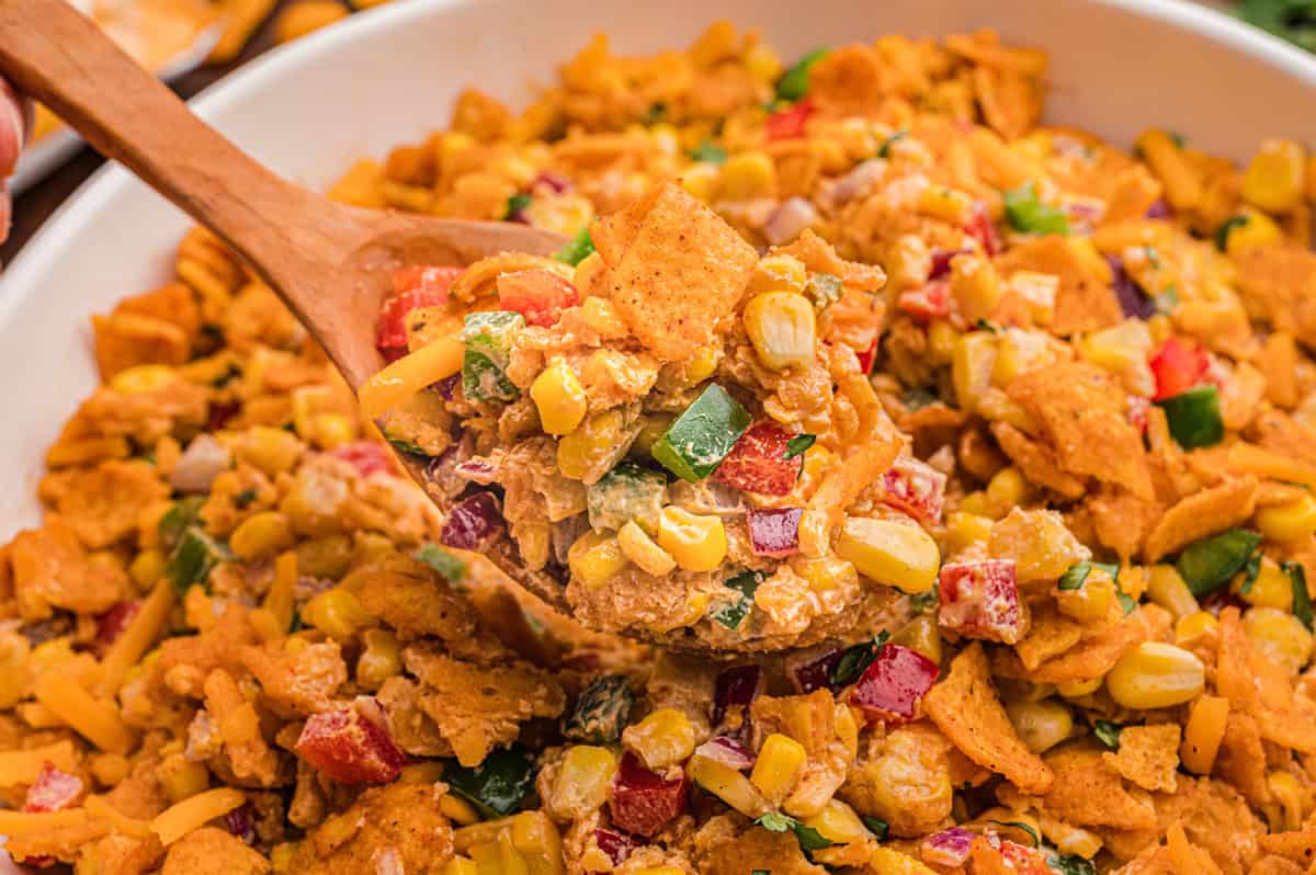 Bowl of Frito corn salad with a wooden spoon.