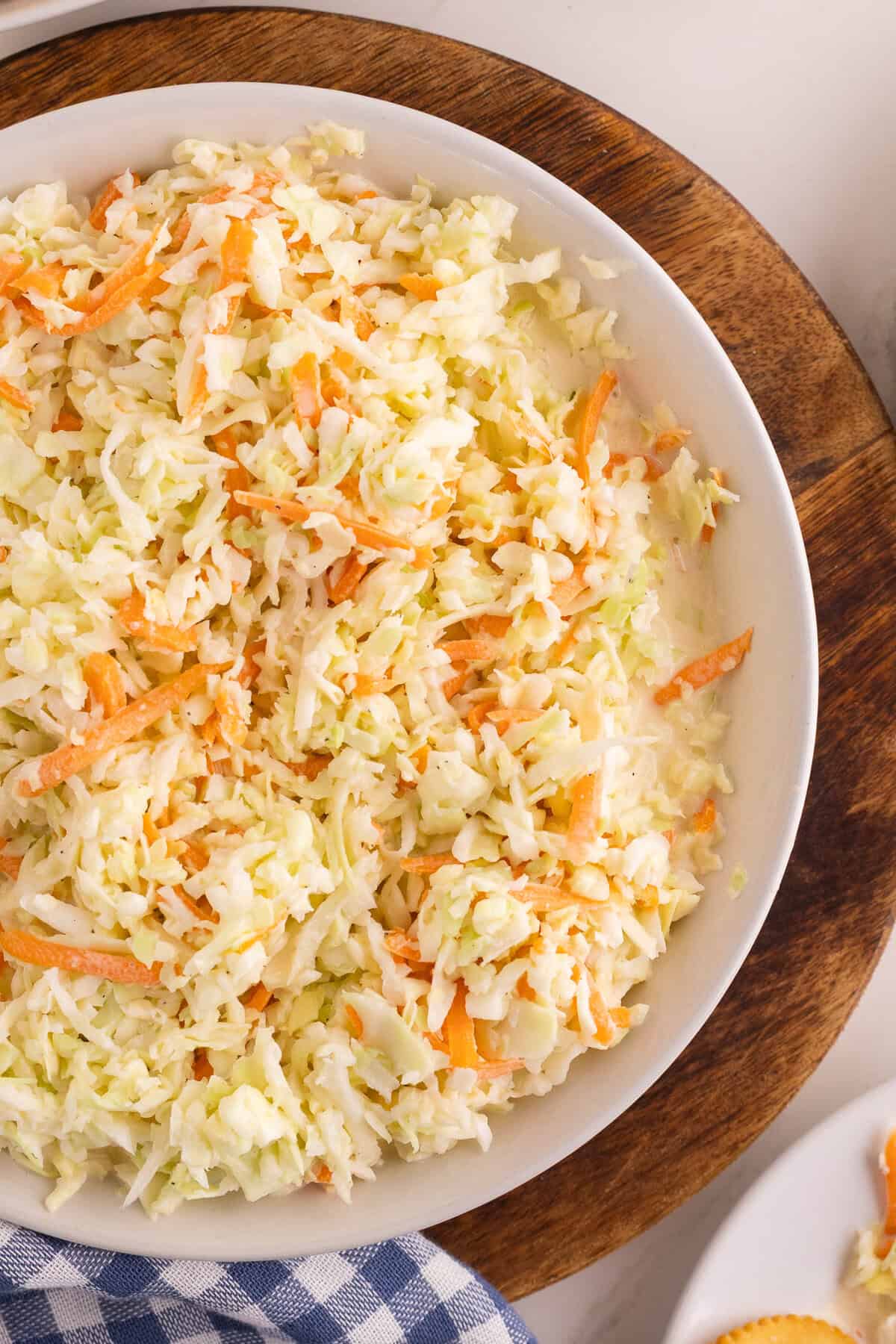 Overhead view of homemade coleslaw in a white bowl with shredded green cabbage and orange carrots tossed in creamy dressing.