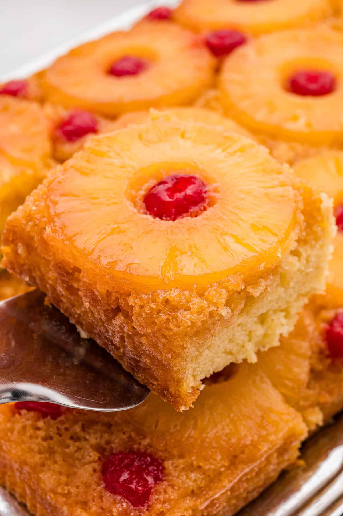 A slice of pineapple upside down cake being lifted on a metal serving spatula from the pan.