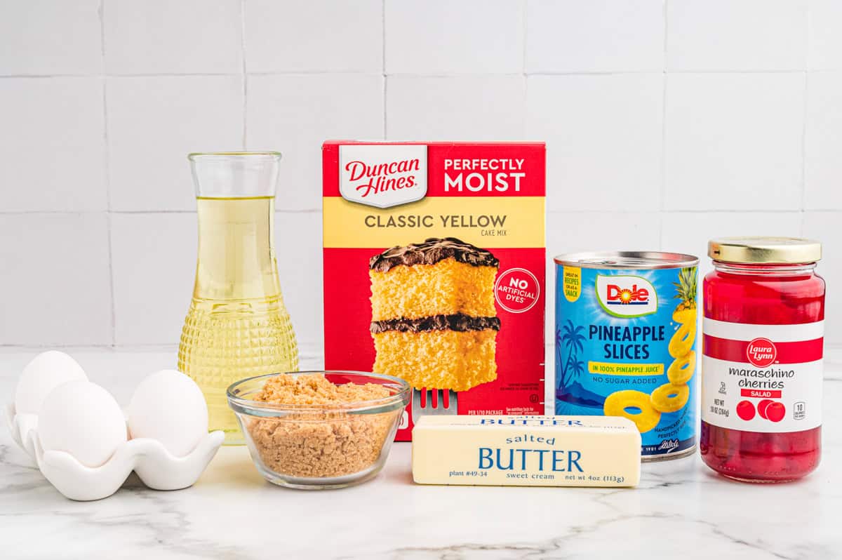 Ingredients for pineapple upside down cake: yellow cake mix, canned pineapple slices, maraschino cherries, butter, brown sugar, and eggs.