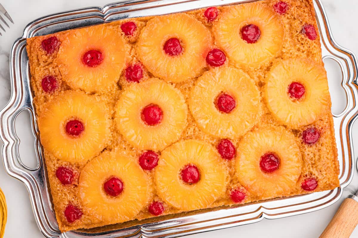 Pineapple upside down cake with cake mix on a white platter, topped with pineapple rings and maraschino cherries.