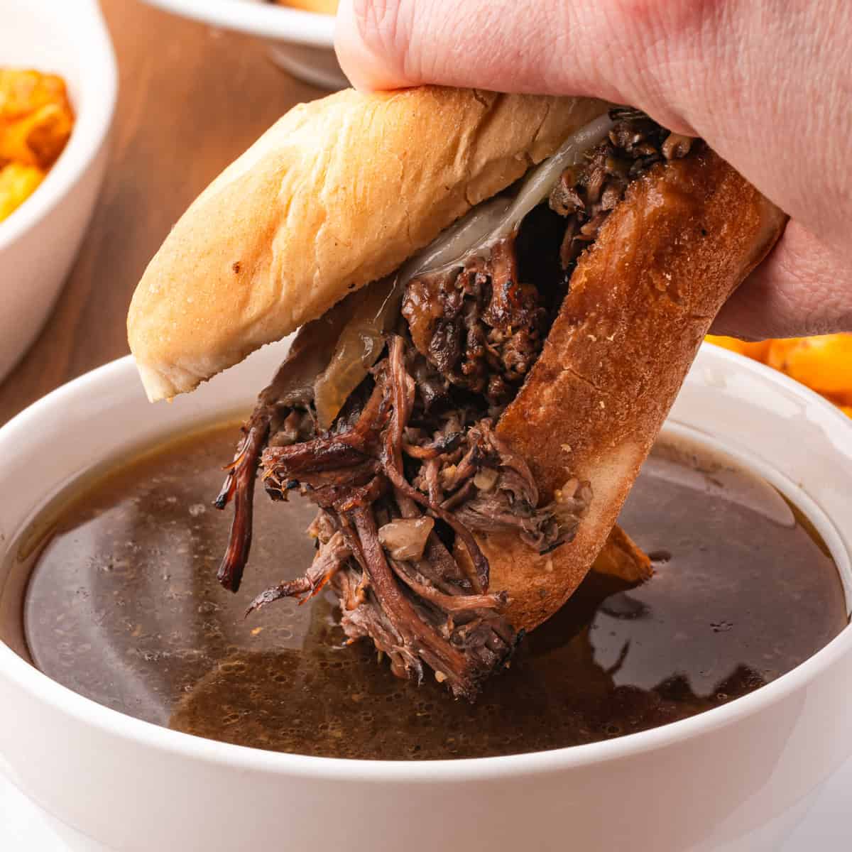 A French Dip Sandwich being dunked into beef au jus.